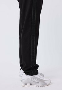 Zwarte joggers met groene zijkanten en een gestructureerd patroon. Gecombineerd met witte Nike sneakers met een zilveren accent en zichtbare stiksels.