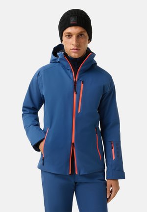 Blue waterproof jacket with orange accents, zipped pockets, a hood, and a textured finish. Paired with a black knit beanie.