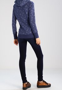 Granatowa bluza z kapturem z wzorem, z przednią kieszenią i ściągaczami na mankietach, w zestawieniu z ciemnymi, dopasowanymi jeansami oraz brązowymi trampkami z czarnymi sznurówkami.