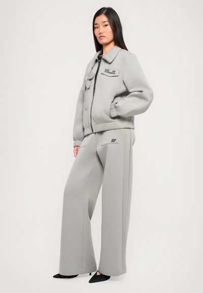 Gray sweater jacket with a zip, ribbed cuffs, and a patch. Paired with gray wide-leg pants featuring a logo on the pocket. Smooth texture.