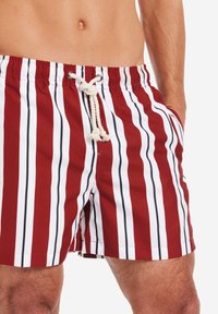 Costume da bagno a righe rosse e bianche con chiusura a cordoncino e dettagli neri. Realizzato in tessuto leggero, presenta tasche laterali.