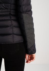 Doudoune avec extérieur matelassé bleu marine, renforts de tissu gris aux coudes et poignets côtelés. Gros plan sur le design du dos et du bras.