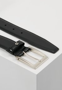 Cinturón de cuero negro con una hebilla rectangular plateada y brillante, que presenta una textura suave y múltiples agujeros de ajuste a lo largo de la correa.