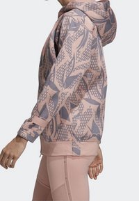 Mikina s kapucí v jemně růžové barvě s modrými geometrickými a listovými vzory. Disponuje uvolněným střihem, žebrovanými manžetami a klokankovou kapsou.