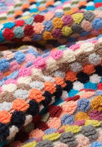 Textured multicolored fabric with hexagonal patterns in shades of pink, blue, orange, and brown; soft, plush yarn construction.