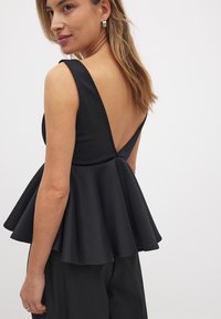 Top peplum nero con schiena a V profonda, realizzato in un tessuto morbido. Presenta spalline larghe e orlo svasato per una silhouette strutturata.