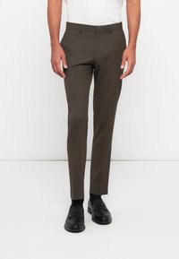 Brown tailored trousers with a slim fit and subtle texture, featuring a belt loop waistband and side pockets, paired with black loafers.