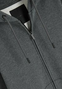 Szara bluza zapinana na zamek, wykonana z mieszanki bawełny, z miękkim wnętrzem i regulowanymi sznurkami. Zawiera czarne akcesoria oraz subtelne logo.