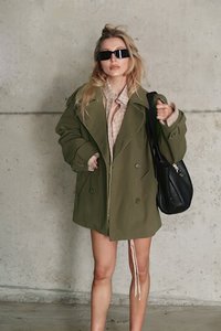 Olive zaļa pārpalikuma mētelis ar dubultā pogojuma aizdari, valkāts virs beigās plānotā krekla. Melni taisnstūra saulesbrilles un liels melns soma.