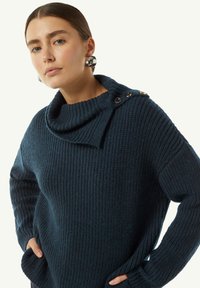 Granatowy sweter dzianinowy z golfem, wyróżniający się prążkowaną teksturą, guzikami na ramieniu oraz bocznymi kieszeniami.