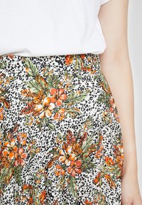 Blommig kjol i vitt, med orange, gula och gröna blommor samt leopardmönstrade detaljer. Lättviktig tyg med en åtsittande midja.