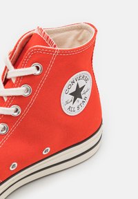 Czerwone płócienne sneakersy za kostkę z białym przeszyciem, otworami na sznurowadła oraz okrągłą naszywką z czarną gwiazdą. Gumowa podeszwa z paskowym wzorem.