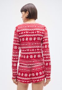 Rdeč praznični dolg rokav z belimi vzorci snežink in jelenov, z okroglim izrezom in rebrastimi manšetami. Ujemajoče kratke hlače.