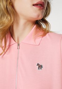 Polo zippé rose en tissu texturé, avec un motif de cheval multicolore brodé sur le côté gauche de la poitrine et un col standard.