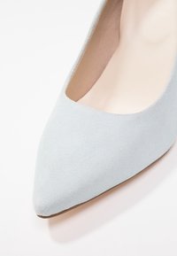 Chaussure plate à bout pointu en daim bleu clair avec une doublure intérieure beige et une semelle lisse visible sur un fond blanc.