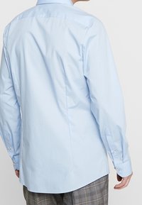 Lichtblauw shirt met lange mouwen, heeft een gladde textuur, standaardkraag en manchetten met knopen, met een rechte snit en subtiele naaddetails aan de achterkant.