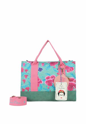 Sac fourre-tout coloré avec motif floral bleu sarcelle et rose, poignées roses, base verte et étiquette attachée représentant un visage stylisé avec des fleurs et du texte.