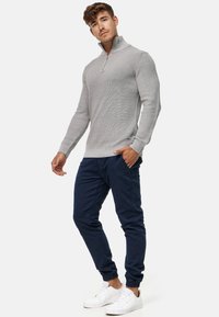 Jasnoszary sweter z ribbowanym wykończeniem i krótkim zamkiem, zestawiony z granatowymi spodniami dresowymi i białymi sneakersami, prezentujący swobodny, dopasowany styl.