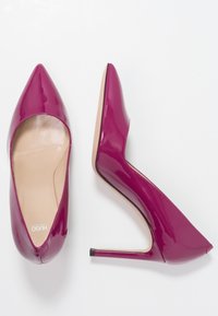 Escarpins à talons hauts en fuchsia brillant avec un bout pointu, une doublure intérieure beige et un talon aigu slim. Texture lisse et design courbé.