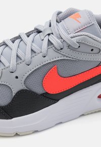 Baskets de sport grises avec une tige en mesh et des accents en cuir noir, ainsi qu'un logo Swoosh orange vif. Comprend des lacets gris et une semelle texturée.