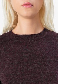 Burgundy knit sweater featuring a round neckline, textured weave, and a soft, fuzzy appearance, with light gray flecks throughout.