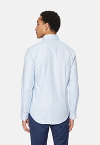 Camisa de cuadros azul claro, de botones, con mangas largas, cuello y dobladillo curvado. Tejido suave con una textura sutil y diseño ajustado.