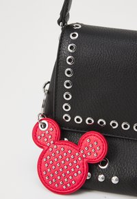 Sac en cuir noir avec des œillets en argent le long du bord, orné d'un charm en forme de Mickey Mouse rouge décoré de clous.