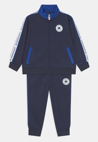 Chándal navy que incluye una chaqueta con cremallera y acentos en azul, bolsillos laterales y logo bordado. Puños y cintura elásticos para mayor comodidad.