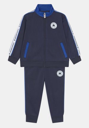 Completo tuta navy con giacca zip-up, dettagli blu, tasche laterali e logo ricamato. Polsi e vita elastici per il massimo comfort.