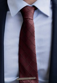 Burgundska kravata s vzorom diamanta, svilen tekstura, s srebrnim zatičem za kravato, nosi se preko svetlo modre srajce in temnega blazerja.