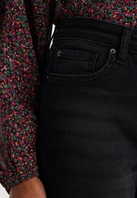 I jeans in denim nero presentano un classico design a cinque tasche con vita alta e finiture metalliche. Il tessuto ha una finitura liscia con una leggera trama.