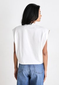 White cropped top with shoulder pads, made of soft cotton. Features a round neckline, casual fit, and straight cut at the hem.