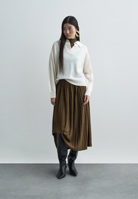 Trui van zachte witte stof met een kraag, gecombineerd met een bruine geplooide midirok en zwarte enkellaarsjes. Eenvoudig ontwerp, zonder patronen.