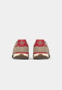 Γκρι σουέτ αθλητικά παπούτσια με κόκκινες λεπτομέρειες και λογότυπο. Μαλακή φτέρνα και λευκή μεσαία σόλα, με εξωτερική σόλα από καφέ ραβδωτό καουτσούκ.