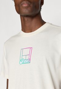 Κρέμ μπλούζα με στρογγυλή λαιμόκοψη και κοντά μανίκια. Διαθέτει πολύχρωμο λογότυπο Asics σε ροζ και τουρκουάζ πάνω στο ύφασμα.