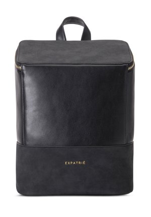 Sac à dos rectangulaire noir avec poignée supérieure, fermeture éclair dorée, et "EXPATRIÉ" embossé en or sur le panneau avant inférieur.