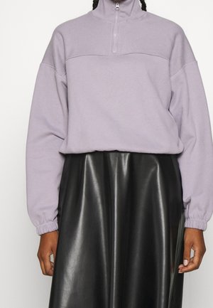 Paarse fleece pullover met hoge kraag en halve rits, gecombineerd met een zwarte leren rok met een gladde, glanzende textuur.