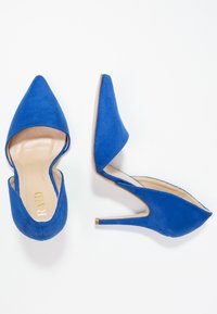 Des escarpins en suède bleu, avec un bout pointu et des côtés ouverts, dotés d'un talon aiguille et d'une semelle intérieure beige lisse.