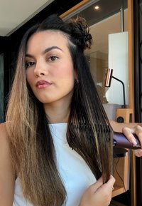 Spazzola per capelli elettrica con un manico viola, setole lunghe e una mano femminile che la tiene. I capelli sono lunghi, lisci e con un effetto ombré che va dal marrone scuro al chiaro.