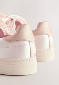 Rosa Satin-Sneaker mit glatter Textur, ausgestattet mit einem absatzbetonten Akzent in zartem Rosaton und einer weißen Gummisohle. Mit gesteppten Details entlang der Kanten.