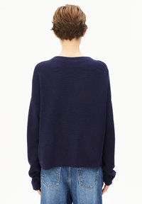 Marineblauwe cropped trui in een geribbelde breistekstuur met verlaagde schouders, gecombineerd met lichtblauwe denimjeans.