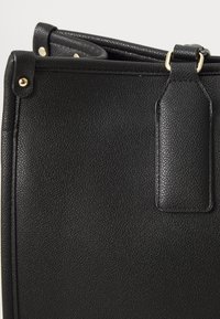 Black handbag made of textured leather with gold-toned hardware, featuring curved edges and a stitched accent near the handle.