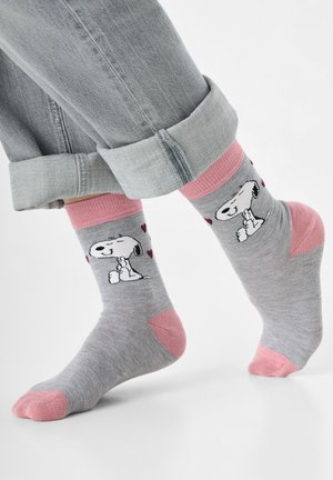 Chaussettes en coton gris avec des accents roses, présentant un motif Snoopy et des motifs de cœurs. Jeans retroussés visibles au-dessus des chaussettes.