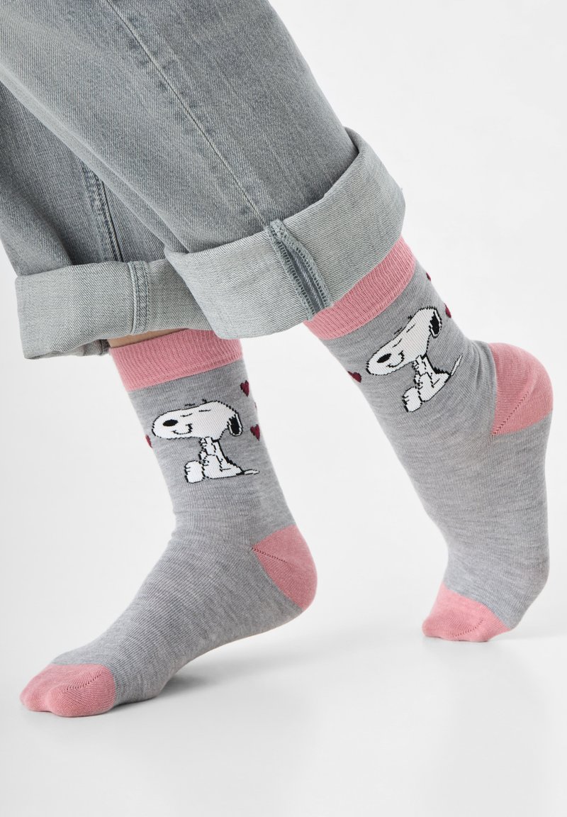 Graue Baumwollsocken mit pinken Akzenten, die ein Snoopy-Motiv und Herzmuster zeigen. Über den Socken sind aufgekrempelte Jeans sichtbar.