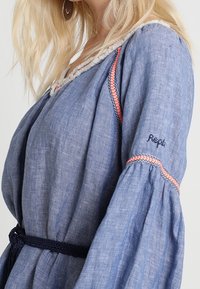 Vaaleansininen pellavapuku, jossa on kellohelmat. Varustettu punaisilla ja tummansinisillä punoksilla kaula-aukon ja hihansuiden ympärillä. Käsinommeltu "Repli" hihassa.
