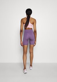 Vaaleanpunainen urheiluliivit ja violetit korkeavyötäröiset shortsit, joissa on sileä pinta, istuva muotoilu ja yhteensopivat vaaleat urheilukengät.