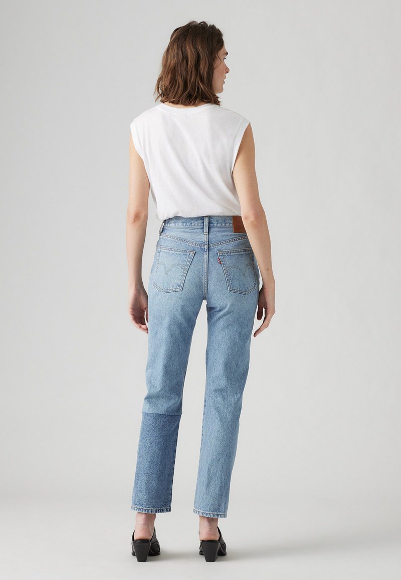 Jeans blu a vita alta con gamba dritta, orlo sfrangiato e tasche posteriori. Abbinati a un top bianco senza maniche. Tacchi neri completano l'outfit.