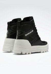 Black high-top sneakers with mesh and leather material, chunky white sole, prominent Reebok logo, and reinforced ankle support.