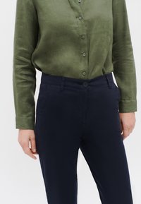 Mörkblå byxor med slim fit, tillsammans med en texturerad olivgrön skjorta med knappar, som har krage och långa ärmar.