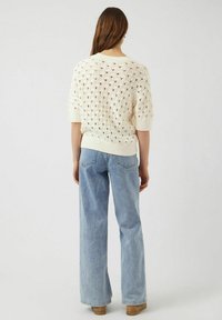 Krämfärgad stickad tröja med diamantmönster, korta ärmar och ribbad nederkant, kombinerad med högmidjade ljusblå jeans.